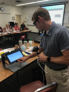 A man stand to the right of frame. To the left of frame, a tablet with OCR scans then reads the text.